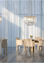 Distant Clérachic chandelier hanging in a tall glass-walled room above a round table with cream chairs and sheer curtains.