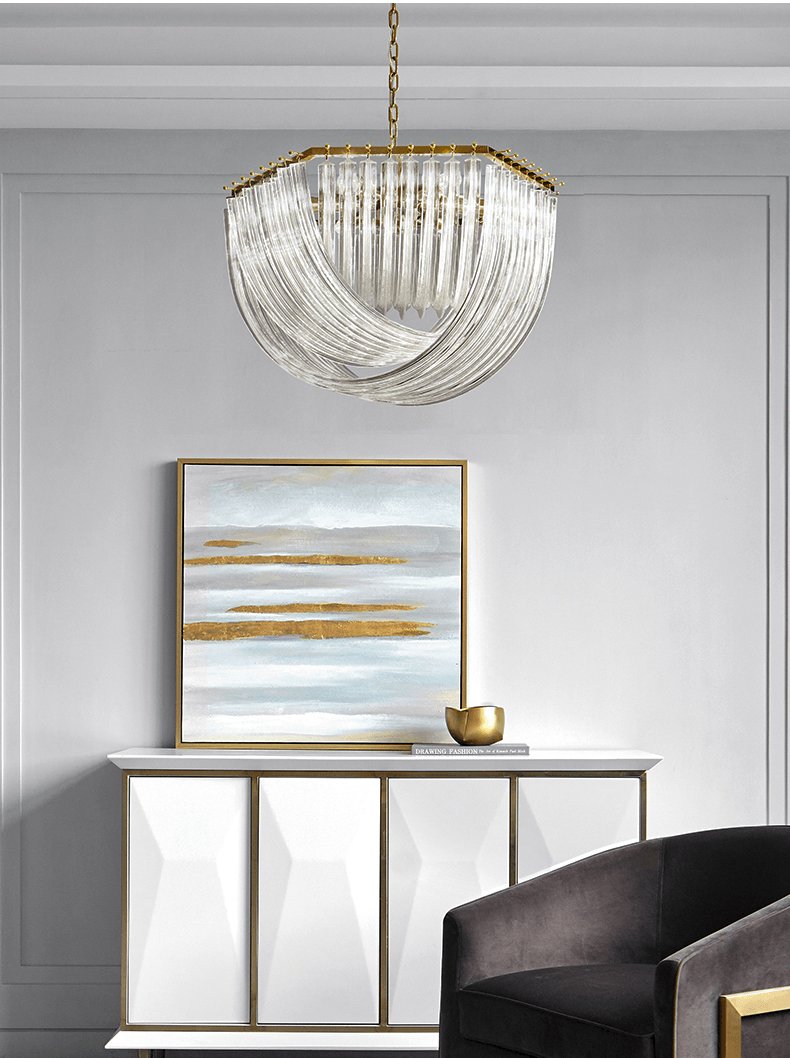Clérachic chandelier above a white sideboard with a gold-and-blue painting, a gold bowl and a dark armchair.