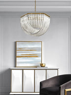 Clérachic chandelier above a white sideboard with a gold-and-blue painting, a gold bowl and a dark armchair.