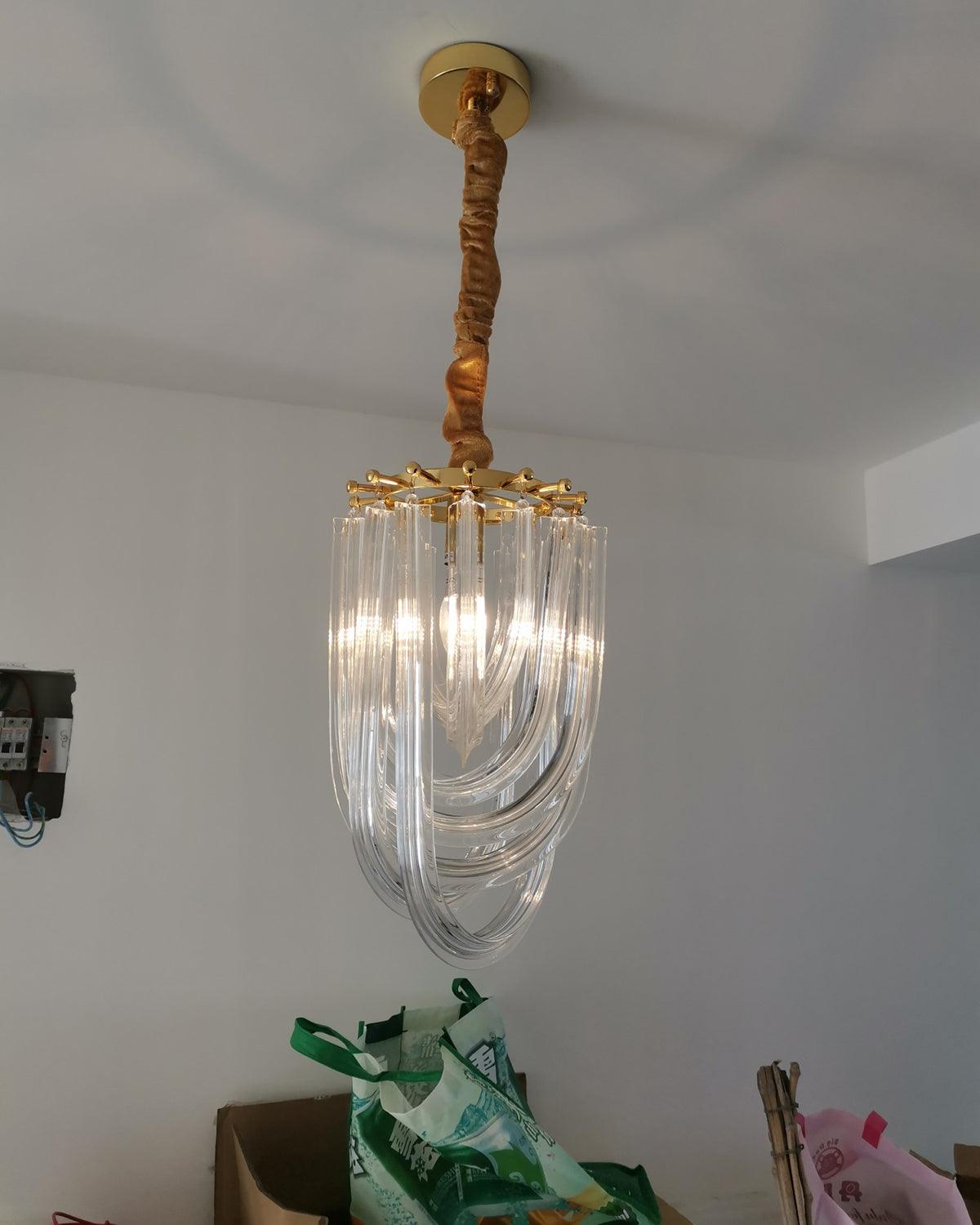 Narrow looped-glass Clérachic chandelier hung from a gold canopy on a twisted fabric cord, with a green bag on the floor below.