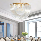Wide Clérachic chandelier with curved clear glass rods above a dining table with glasses, flowers and two blue paintings behind.