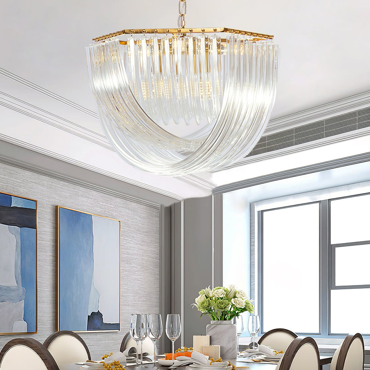 Wide Clérachic chandelier with curved clear glass rods above a dining table with glasses, flowers and two blue paintings behind.