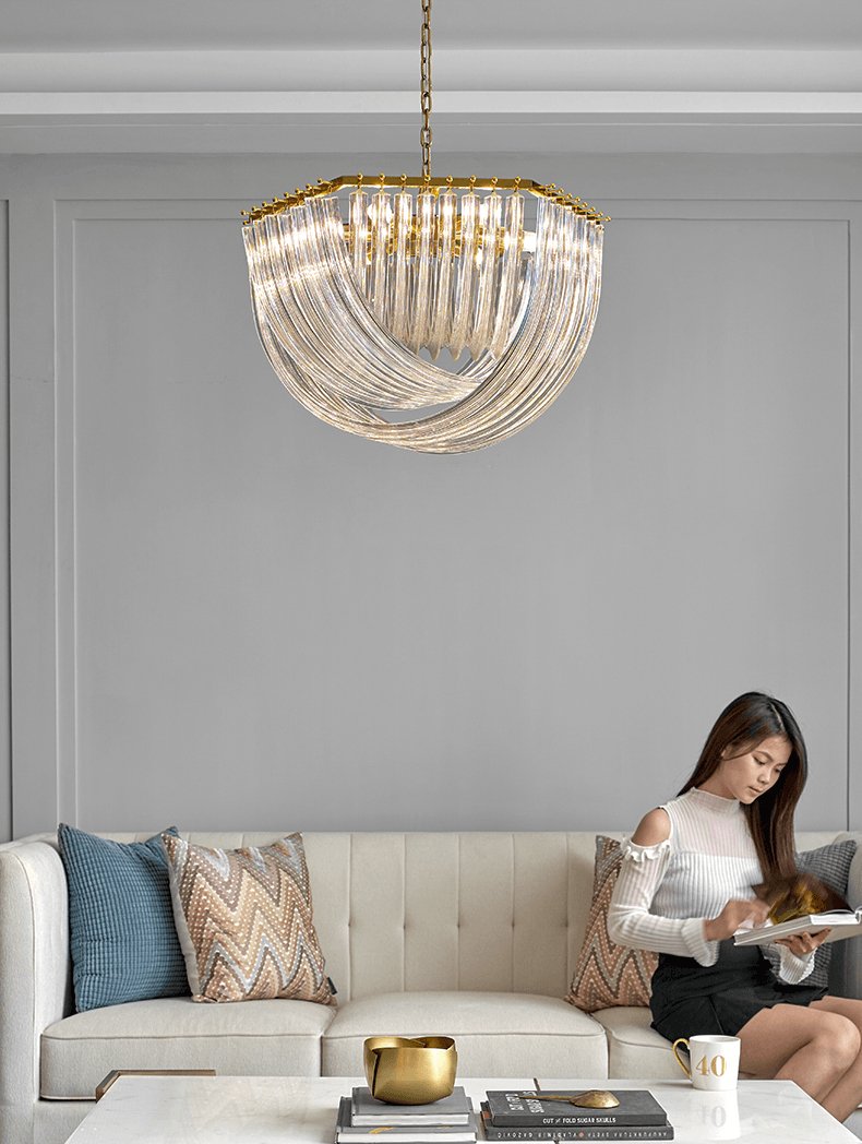 Clérachic chandelier on a chain above a cream tufted sofa, where a woman sits reading, against a grey panelled wall.