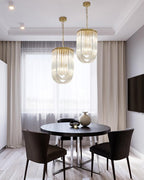 Two narrow looped-glass Clérachic chandeliers hung at different heights over a round dark dining table with brown chairs.
