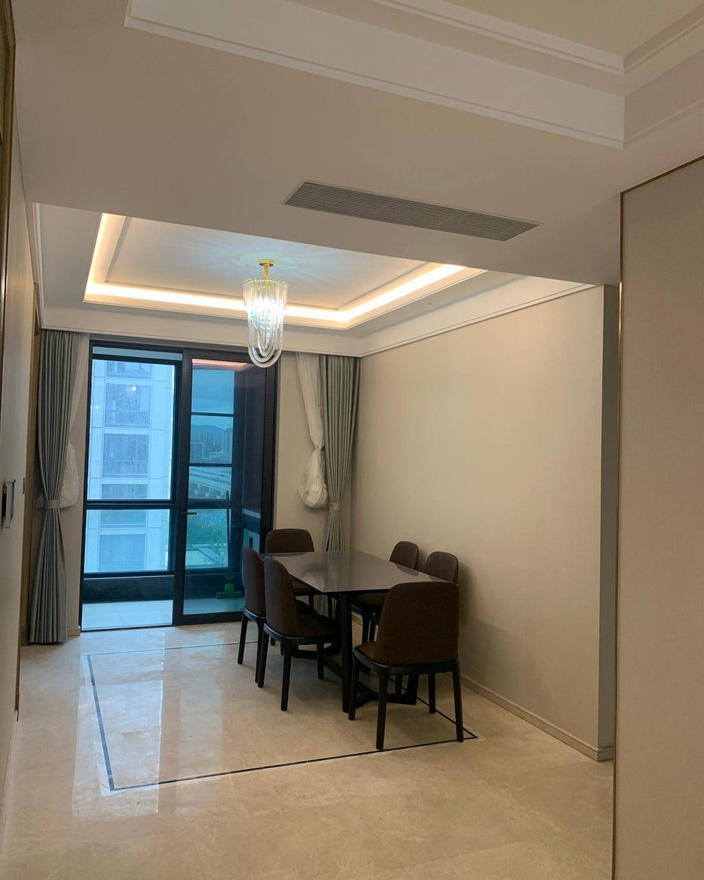 Small Clérachic chandelier seen far off, hung in a pale room with a cove-lit ceiling and a dining table by a window.