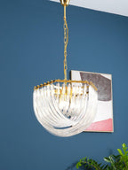 Clérachic chandelier on a gold chain against a blue wall, its looped clear glass rods lit beside an abstract picture.