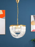 Unlit Clérachic chandelier on a gold chain in front of a blue wall with orange and cream abstract pictures.