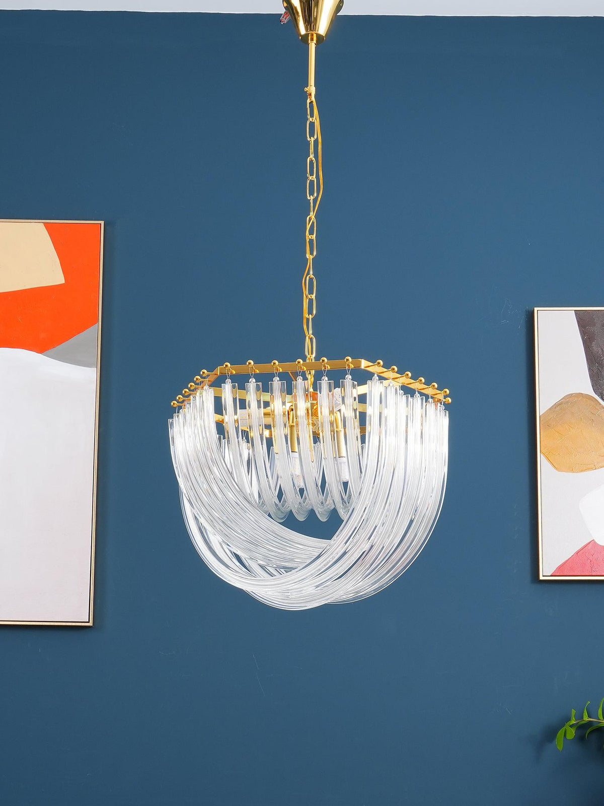 Clérachic chandelier with looped clear glass rods and a gold hexagonal top, hung against a blue wall with abstract art.