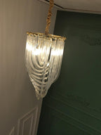 Narrow looped-glass Clérachic chandelier lit and seen from below, with a fabric-wrapped cord and a green panelled wall.
