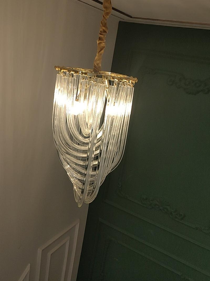 Narrow looped-glass Clérachic chandelier lit and seen from below, with a fabric-wrapped cord and a green panelled wall.