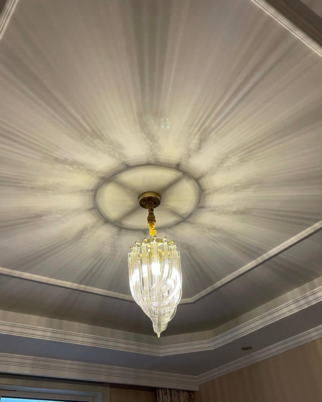 Small Clérachic looped-glass pendant lit below a moulded ceiling, with light rays from the glass cast across the ceiling.