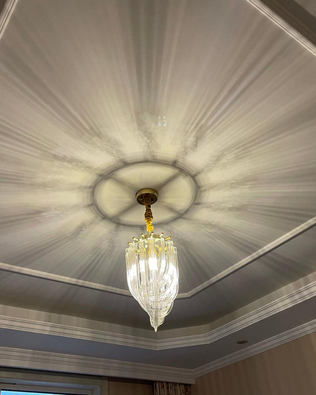 Small Clérachic looped-glass pendant lit below a moulded ceiling, with light rays from the glass cast across the ceiling.