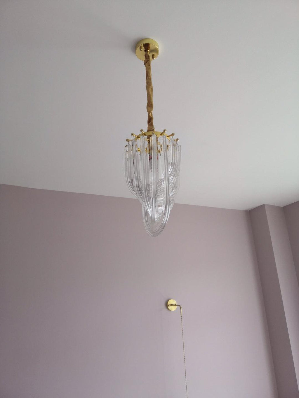 Narrow Clérachic chandelier seen far up, hanging from a cord in a tall room with a lilac wall and a pull cord beside it.