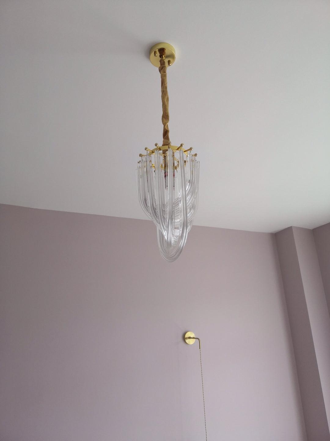 Narrow Clérachic chandelier seen far up, hanging from a cord in a tall room with a lilac wall and a pull cord beside it.