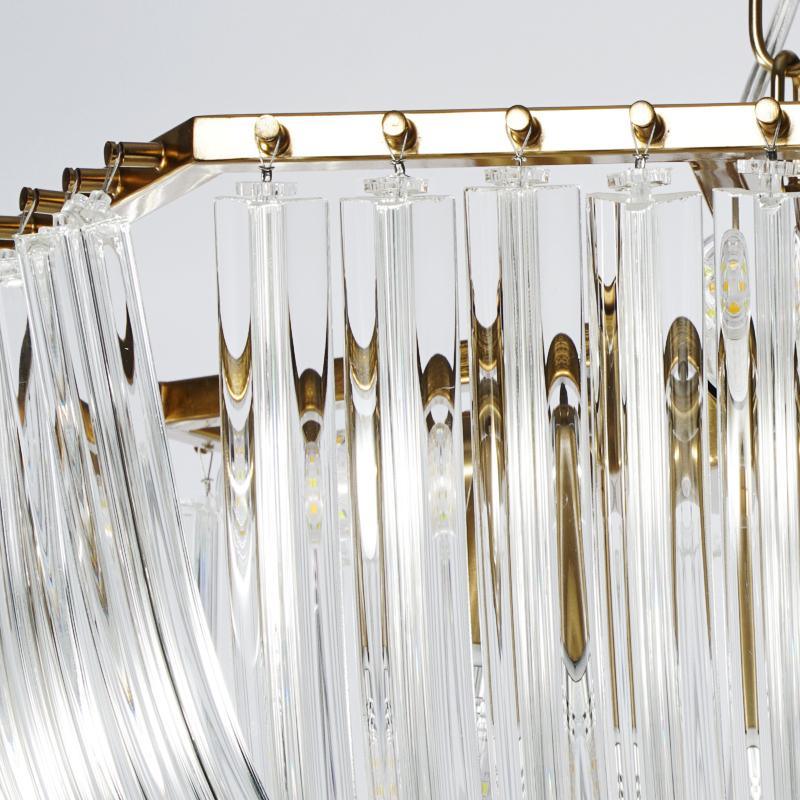 Close view of the gold frame, small gold balls and the hanging clear glass rods along the top of this Clérachic chandelier.