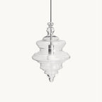 Clear glass pendant with stacked, tiered rings and a pointed tip hanging from a thin cord, on a plain white backdrop from Clérachic.