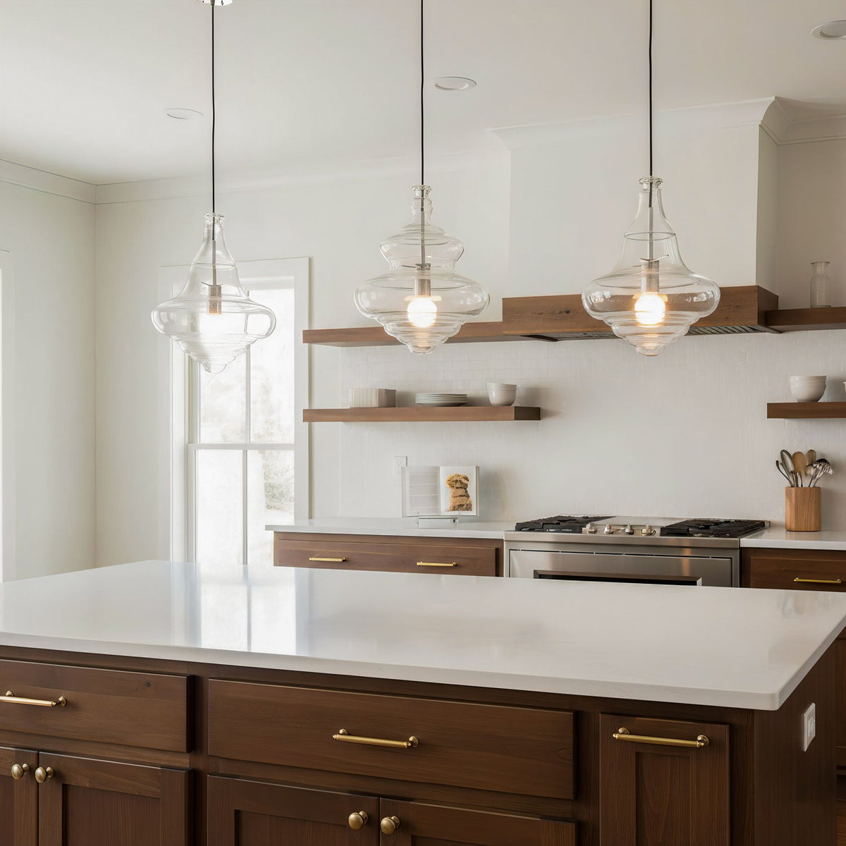 Three Clérachic glass pendants hang above a white kitchen island, with dark wood cabinets and floating shelves in the background.