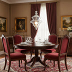 Clear glass Clérachic pendant with a lit bulb hangs above a round dining table with red velvet chairs and heavy red curtains.