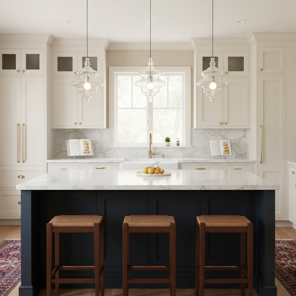 Three clear glass pendants from Clérachic hang in a row over a navy kitchen island with white worktops and woven stools.
