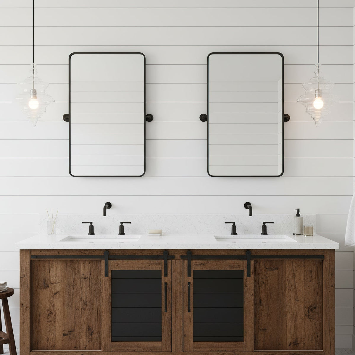 Clear glass pendants from Clérachic hang at both sides of a double vanity, beside two black-framed mirrors on a white boarded wall.