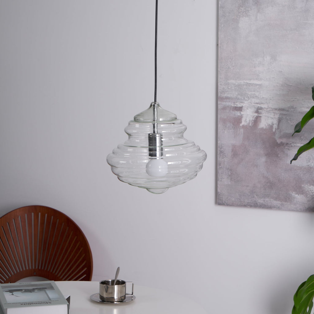 Ribbed clear glass pendant from Clérachic, unlit with a white bulb visible inside, in front of a soft grey painting.
