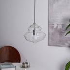 Ribbed clear glass pendant from Clérachic, unlit with a white bulb visible inside, in front of a soft grey painting.