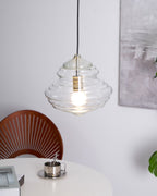 Ribbed Clérachic pendant in clear glass, lit above a white table with a metal cup, with a wooden fan-backed chair beside it.