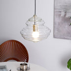 A wide, ribbed Clérachic glass pendant glows above a table, its cord dropping from the top of the frame.