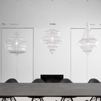 Three clear glass Clérachic pendants in different shapes hang above a long grey table with black chairs, in a white room.