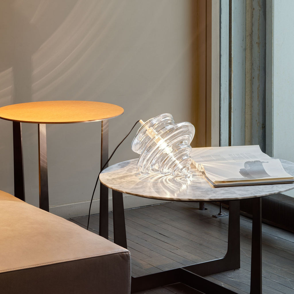 Ribbed clear glass Clérachic shade resting on a marble coffee table beside an open magazine, with a round side table behind.