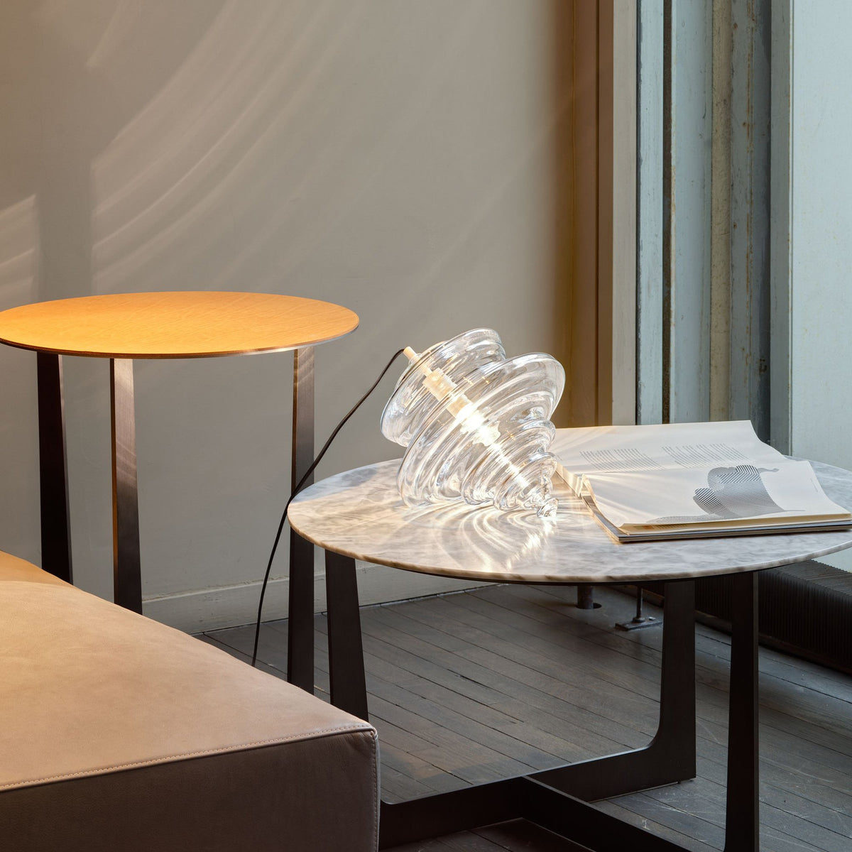 Ribbed clear glass Clérachic shade resting on a marble coffee table beside an open magazine, with a round side table behind.