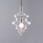 A lit, tiered clear glass pendant from Clérachic on a grey backdrop, showing a pointed tip and a black cord.