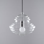 Wide, ribbed clear glass pendant from Clérachic with an unlit bulb and silver-toned holder, on a grey backdrop.