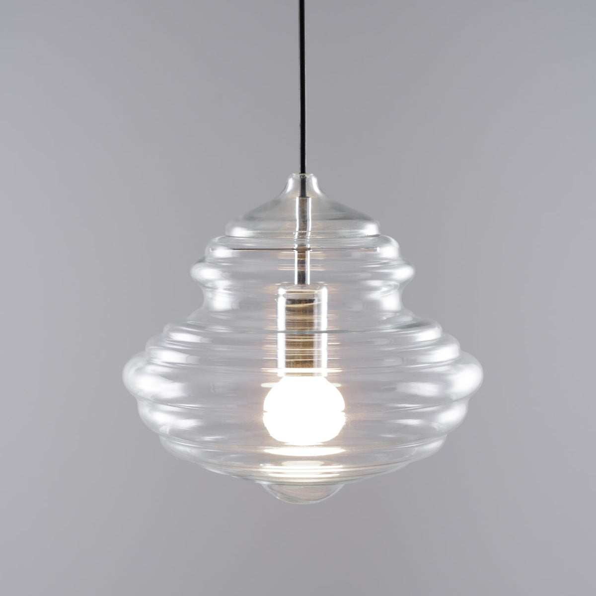 Ribbed Clérachic glass pendant lit warm, on a plain grey backdrop, with horizontal rings running down the shade.