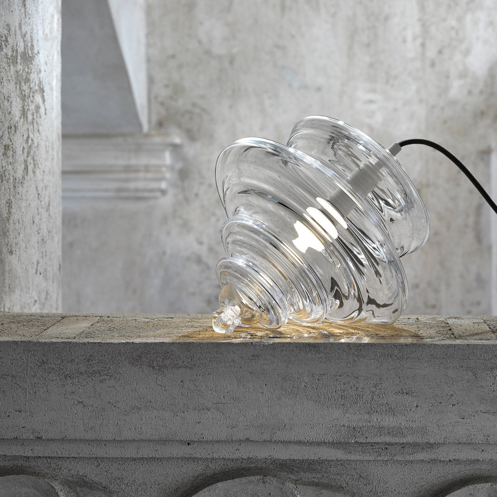 A ribbed clear glass Clérachic shade placed on its side on a concrete ledge, with its black cord trailing to the right.