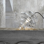 A ribbed clear glass Clérachic shade placed on its side on a concrete ledge, with its black cord trailing to the right.
