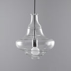 Bell-shaped clear glass pendant from Clérachic with an unlit bulb visible inside, on a grey backdrop.