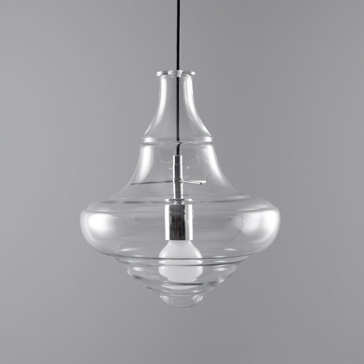 Bell-shaped clear glass pendant from Clérachic with an unlit bulb visible inside, on a grey backdrop.