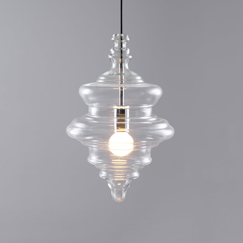 Tiered clear glass pendant from Clérachic lit warm on a grey backdrop, with a small finial at the top and a pointed tip.