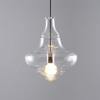 A Clérachic bell-shaped glass pendant with a warm lit bulb, seen at a slight angle against a grey backdrop.