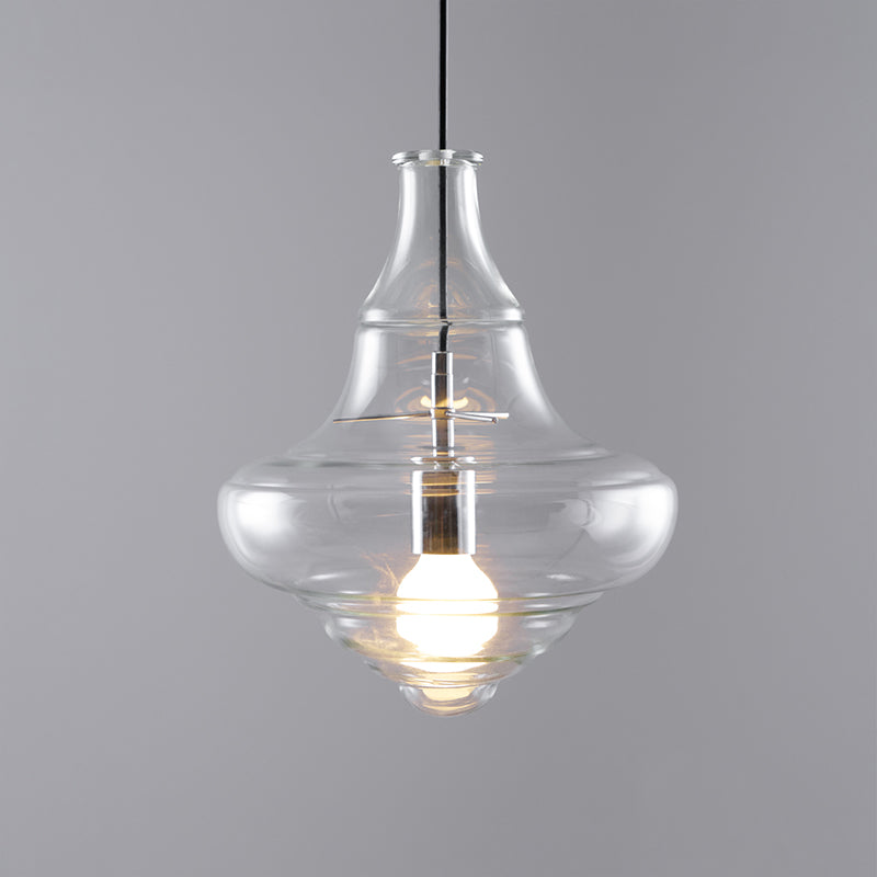 A Clérachic bell-shaped glass pendant with a warm lit bulb, seen at a slight angle against a grey backdrop.