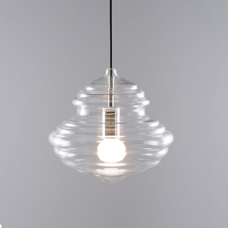 Wide ribbed clear glass Clérachic pendant, with a black cord and a softly lit bulb, on a grey backdrop.