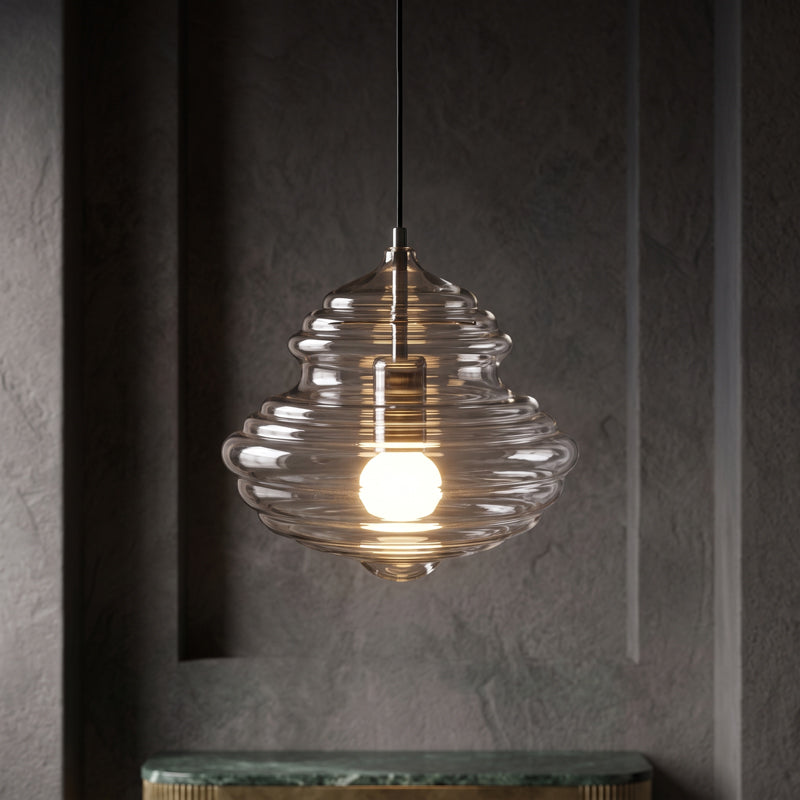 Ribbed clear glass Clérachic pendant glowing warm in a dark grey alcove, above the edge of a green marble shelf.