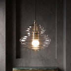 Ribbed clear glass Clérachic pendant glowing warm in a dark grey alcove, above the edge of a green marble shelf.