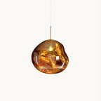 This Clérachic pendant light on a plain white backdrop, in gold, with a glossy, irregular molten-looking glass shade and a slim brass rod.