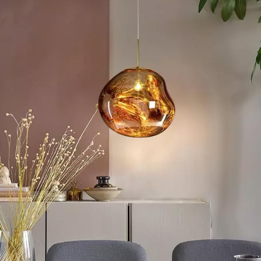 A single Clérachic gold glass pendant by a pink wall, with a vase of dried grasses and a pale sideboard below it.