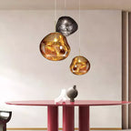 A Clérachic gold glass pendant lit beside a smoke-grey one and a smaller gold one, above a round red table.