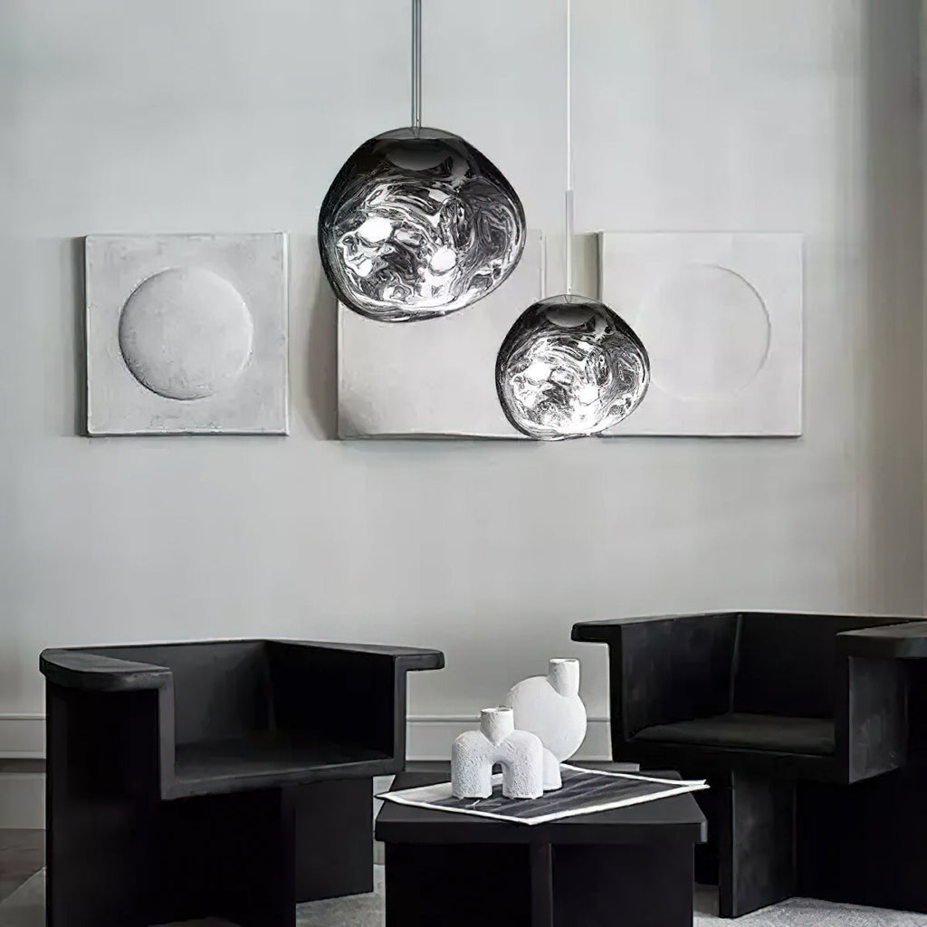 Two Clérachic silver mirror-glass pendants hang in front of grey plaster panels, above two black armchairs and a low table.