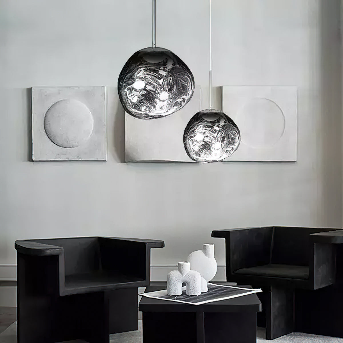 Two Clérachic silver mirror-glass pendants hang in front of grey plaster panels, above two black armchairs and a low table.