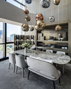 A tall group of Clérachic glass pendants in copper, gold and silver hangs over a marble dining table in a city apartment.
